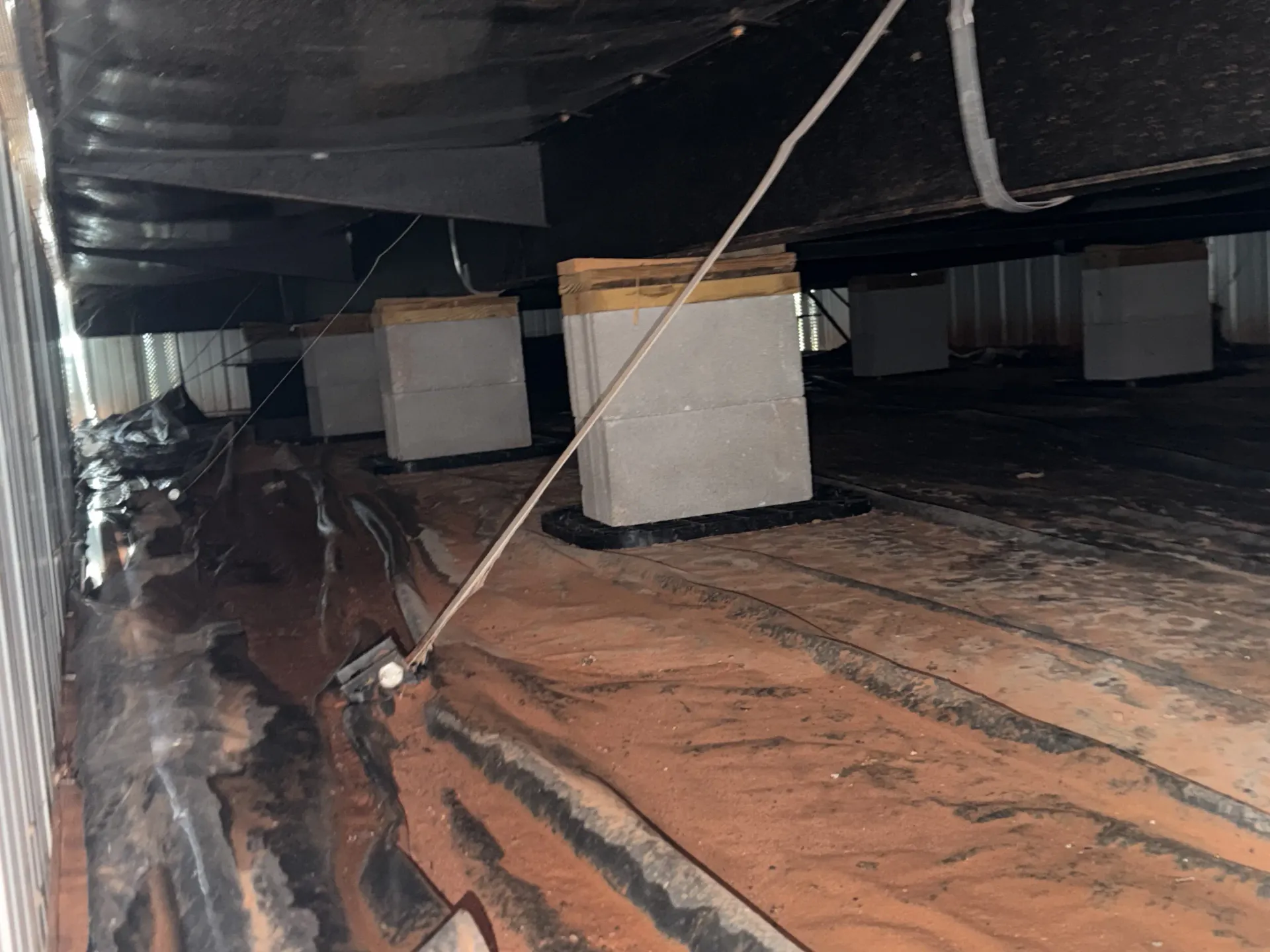 Concrete piers, shims and an anchor tie-down strap under a manufactured home during a HUD foundation inspection